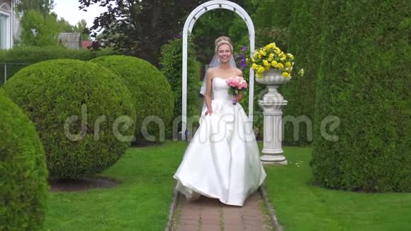 美丽的新娘穿着白色连衣裙带着花束来到花园微笑着视频的预览图