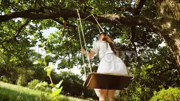 秋天在公园的橡树下一个留着白发的女孩骑着秋千从后面看慢动作视频的预览图
