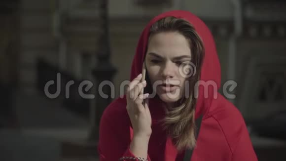 穿着红色运动衫的年轻女孩在电话里讲话视频的预览图