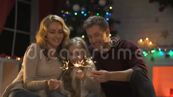 一家人抱着孟加拉灯坐在圣诞树下灯光闪闪发光视频的预览图