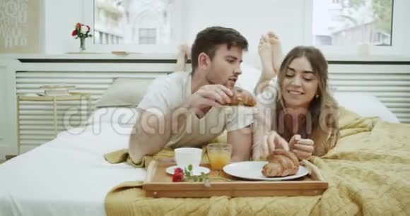 早上一对可爱的夫妇在床上吃早餐吃法式牛角面包聊一聊非常舒适视频的预览图