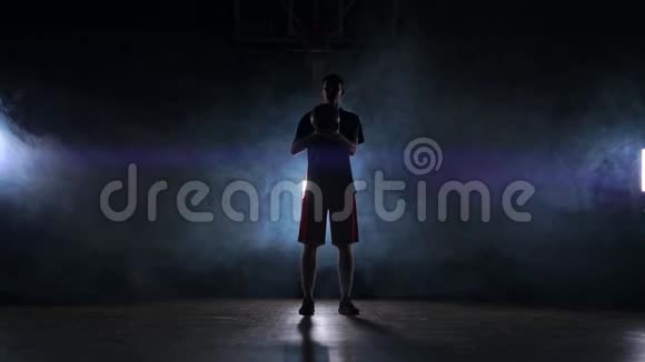 篮球运动员表演不同的技巧和旋转球在黑暗的健身房与烟雾慢动作视频的预览图