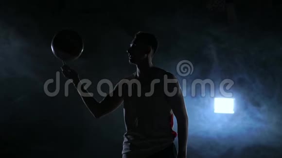 篮球运动员表演不同的技巧和旋转球在黑暗的健身房与烟雾慢动作视频的预览图
