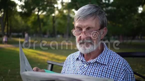 穿格子衬衫的老人坐在公园的长凳上看报纸视频的预览图