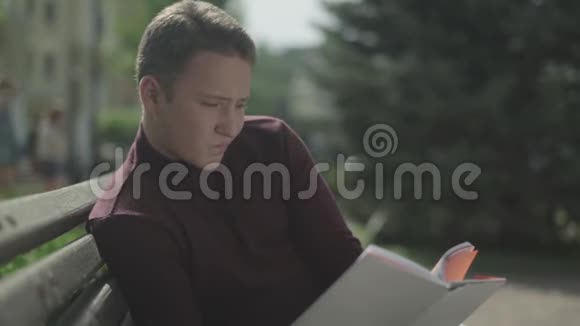 帅哥在公园里仔细地读一本书视频的预览图