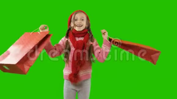 一个十岁左右的女孩戴着一顶红色针织帽子和围巾手里拿着辫子和袋子挥舞着它们为新年感到高兴视频的预览图