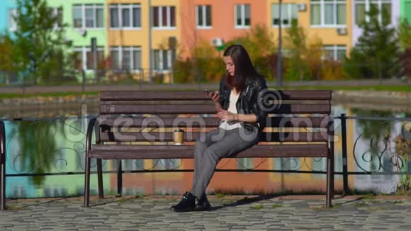 坐在长凳上的女孩在湖边在你的智能手机上读着一条信息笑打印信息视频的预览图
