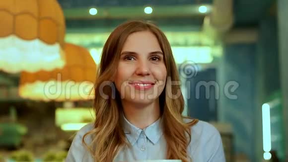 美女喝着杯中的卡布奇诺咖啡对着镜头微笑视频的预览图