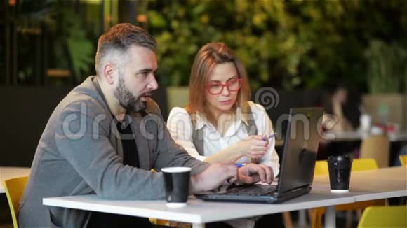 两位年轻的专业人士坐在办公桌前看着笔记本电脑屏幕一起讨论项目男子和妇女工作视频的预览图