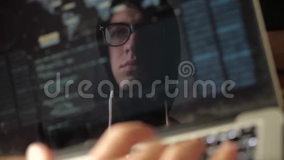 双重曝光戴眼镜的黑客在笔记本电脑上工作黑客写蓝色代码在监视器中反射视频的预览图