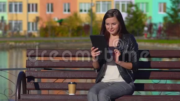 公园里的女孩坐在长凳上拿着平板电脑看着社交网络视频的预览图