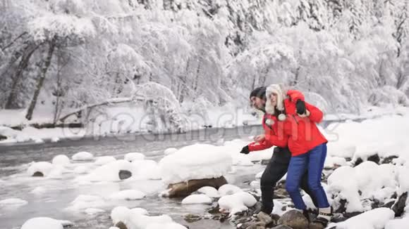 一个年轻幸福的家庭站在一条山河的河口恋爱中的情侣把鹅卵石扔进河里视频的预览图