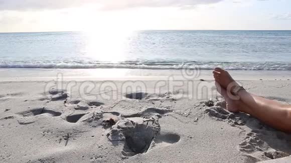 黎明时分一个年轻女子在风中坐在海边的腿上阳光反射在平坦的海水上视频的预览图