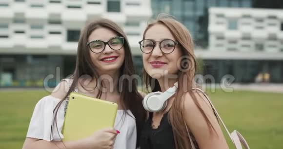 两个快乐的白种人年轻女性最好的朋友一起玩戴着时髦的太阳镜在户外摆姿势看着相机视频的预览图