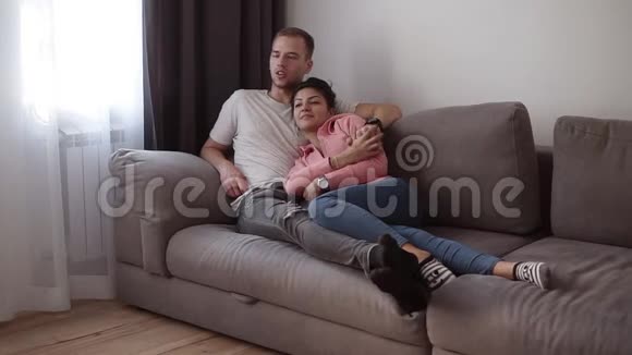 放松的年轻夫妇躺在家里的灰色沙发上客厅里有阁楼里面有电视视频的预览图