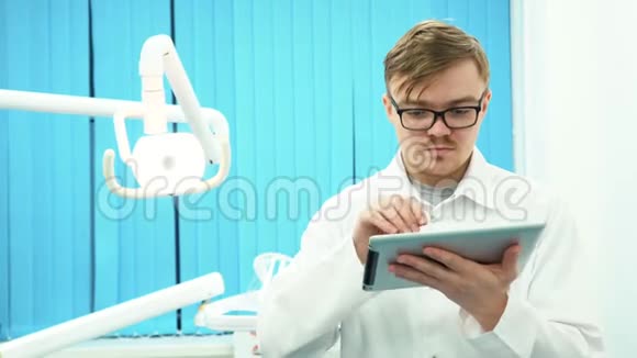 穿着白色外套的年轻牙医在牙科办公室里看着他的药片牙科护理视频的预览图