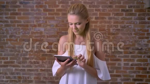 年轻可爱的白种人金发女人用平板电脑滑动显示绿色屏幕就像标志砖墙的背景视频的预览图