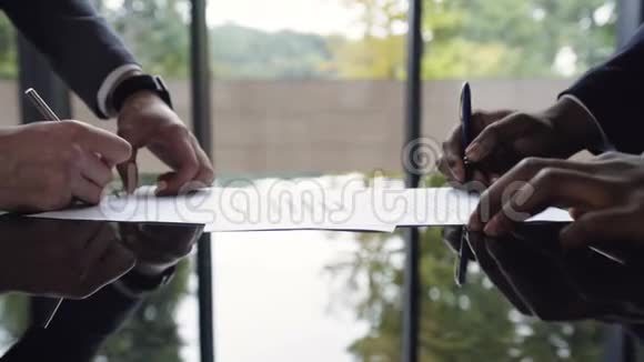 特写镜头两个自信的商人非裔美国人和高加索人在一次会议上握手并签署了协议视频的预览图
