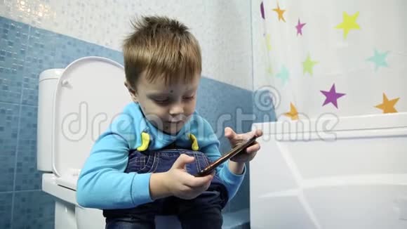 一个小男孩在锅里小便看着电话一个患有水痘的男孩坐在厕所里看着电话视频的预览图