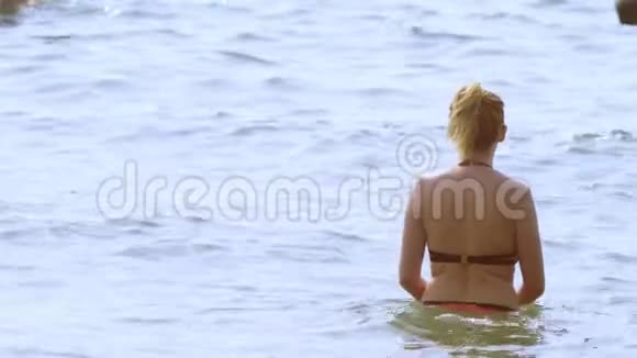 穿着泳衣和黑色太阳镜的金发女孩穿着红色泳衣的女人走进大海视频的预览图