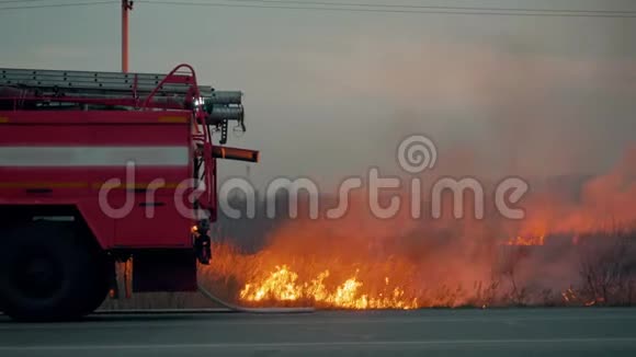 背景燃烧草地上有闪光灯的消防车在野外烧草背景下的消防车视频的预览图