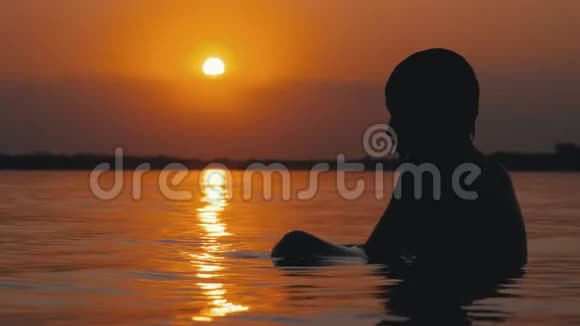 日落和橙径背景下坐在水里的男孩剪影慢动作视频的预览图