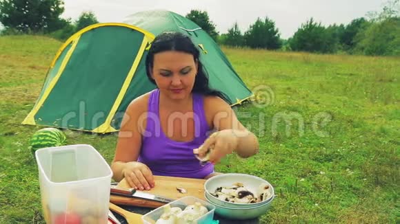 在一张木桌旁的帐篷附近一个女人把切碎的蘑菇涂在盘子上做汤视频的预览图
