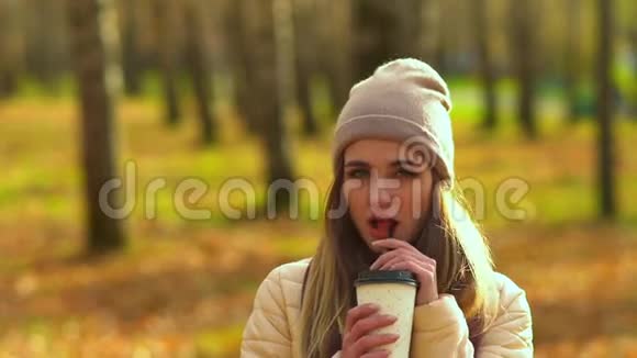 秋天公园里美丽的女孩看着相机喝着咖啡笑着做着脸视频的预览图