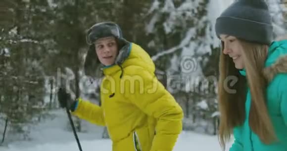 一对已婚夫妇的肖像冬天一个穿黄色夹克的男人和一个穿蓝色连衣裙的女人在树林里滑雪视频的预览图