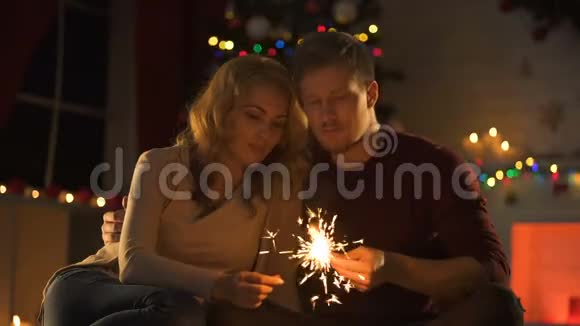 有着孟加拉灯的可爱情侣在闪闪发光的圣诞树旁温柔地接吻视频的预览图
