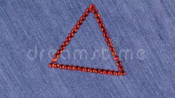 在牛仔布上旋转一个由红色莱茵石制成的三角形三角形象征着完成视频的预览图