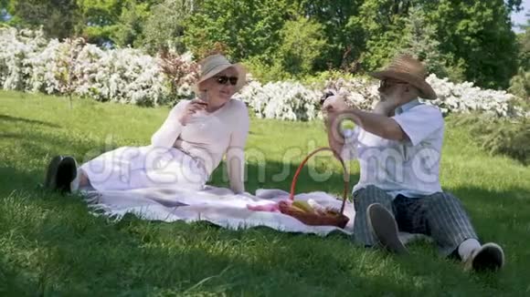 戴帽子的老人在野餐时用一杯酒给他优雅的妻子拍照视频的预览图