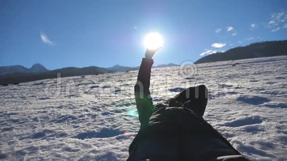 一个面目全非的人躺在雪地上在阳光明媚的日子里用手指望着灿烂的太阳年轻的手视频的预览图