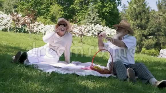 戴帽子的老人在野餐时用一杯酒给他优雅的妻子拍照视频的预览图
