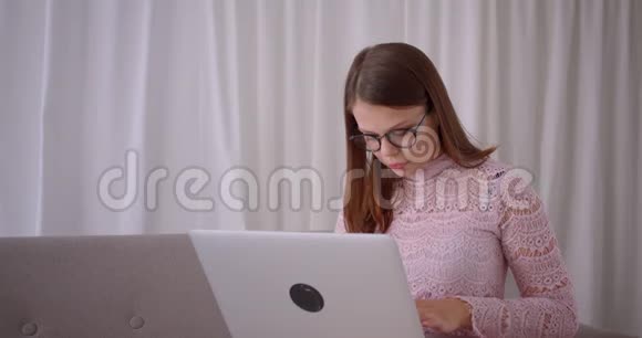 年轻迷人的高加索女商人坐在公寓里的沙发上用笔记本电脑打字的特写照片视频的预览图