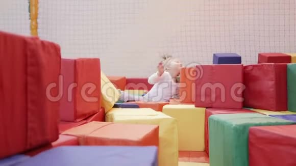 小女孩在游戏室里玩孩子在大的柔软明亮的立方体中爬行视频的预览图