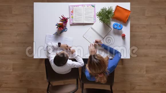 年轻的母亲帮助儿子学习女人写东西给孩子看坐在桌子后面孩子在做视频的预览图