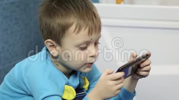 一个小男孩在锅里小便看着电话一个患有水痘的男孩坐在厕所里看着电话视频的预览图
