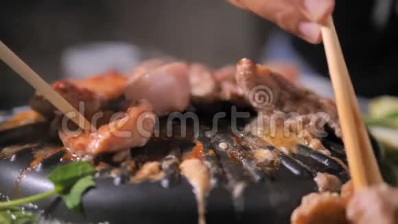 人们用筷子做饭捡猪肉翻猪肉在火锅上用深色和谷物的方法迎接韩国烧烤视频的预览图