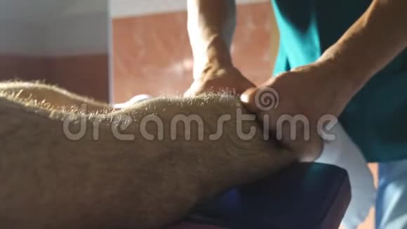 专业按摩师的双臂在沙龙里躺在按摩台上慢慢按摩运动员的腿部男性手视频的预览图