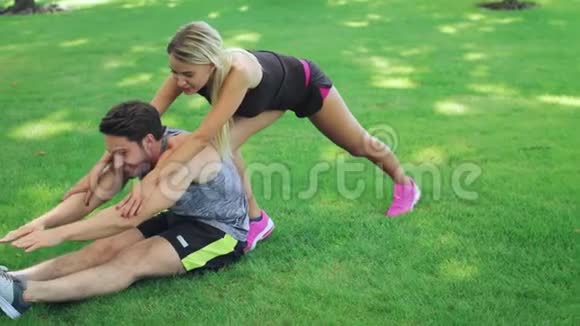 女子运动教练帮助健身男子伸展腿部夏季公园视频的预览图