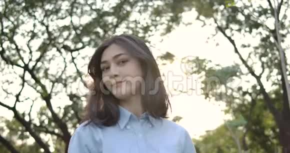 年轻迷人的亚洲女人的肖像在夕阳下的夏日公园里开心地微笑着进入镜头视频的预览图