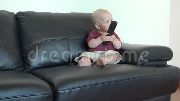 可爱的小男孩坐在黑色沙发上家里有遥控器视频的预览图