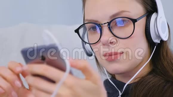 女人在智能手机上用耳机听音乐面部特写视频的预览图