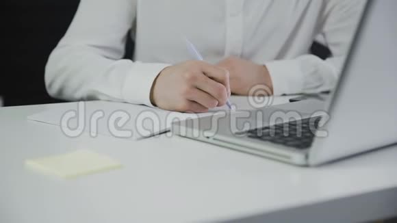 聪明的高加索商人使用笔记本电脑并在记事本上写下信息视频的预览图