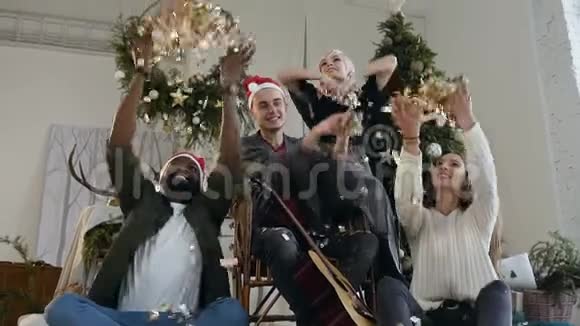 两个穿着圣诞老人帽子的英俊小伙子和他们的女朋友在庆祝新时扔了金色的纸屑视频的预览图