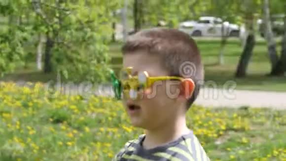 眼镜上的旋转器在旋转在街上玩得很开心黄色花朵背景上的男孩蒲公英视频的预览图