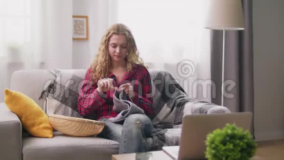 坐在沙发上在舒适的家里编织钩针衣服的女士手持镜头视频的预览图