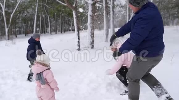 爸爸妈妈儿子和小女儿在下雪天在树林里玩雪球友好的时尚家庭乐趣视频的预览图