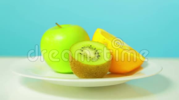 一个完整的绿色苹果和半个猕猴桃和橘子在一个白色的盘子里旋转成一个圆圈视频的预览图